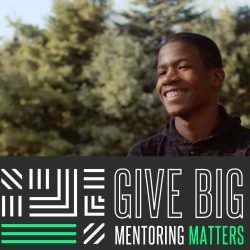 Kevin is smiling outside, above a banner that says "Give Big, Mentoring Matters"