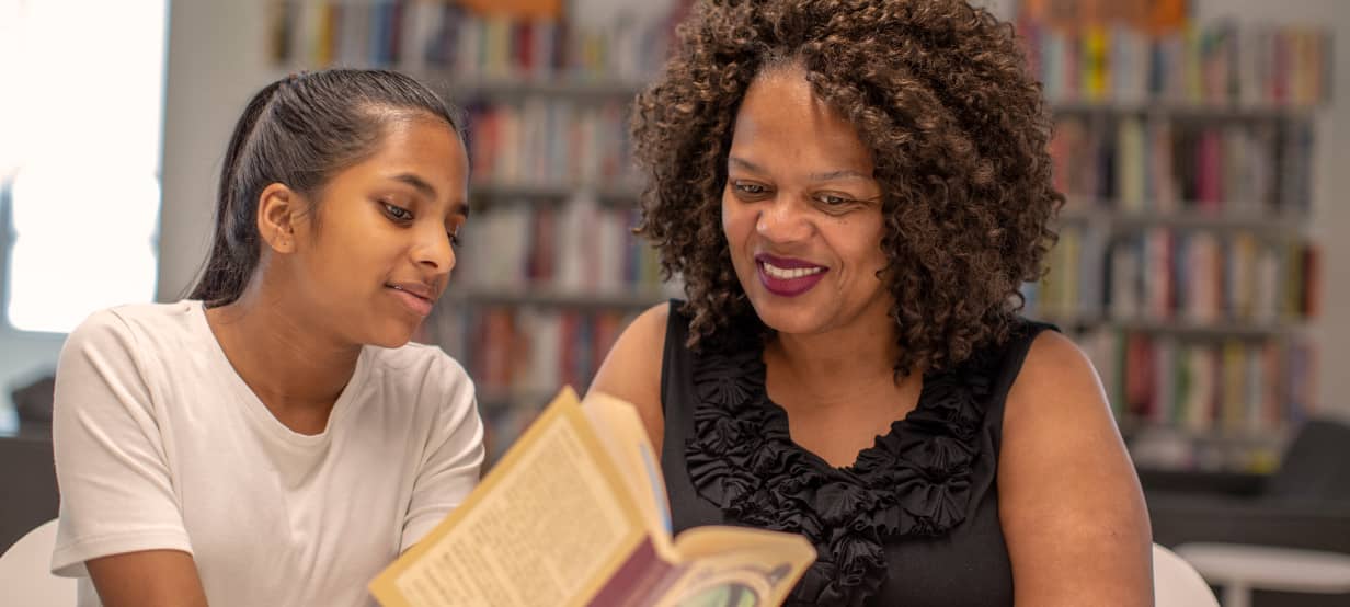 Woman and teenage girl looking at a book together in a library.