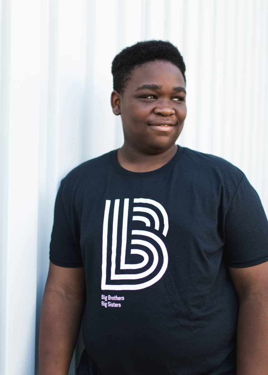 A teenage little in a Big Brothers Big Sisters shirt looks away from the camera
