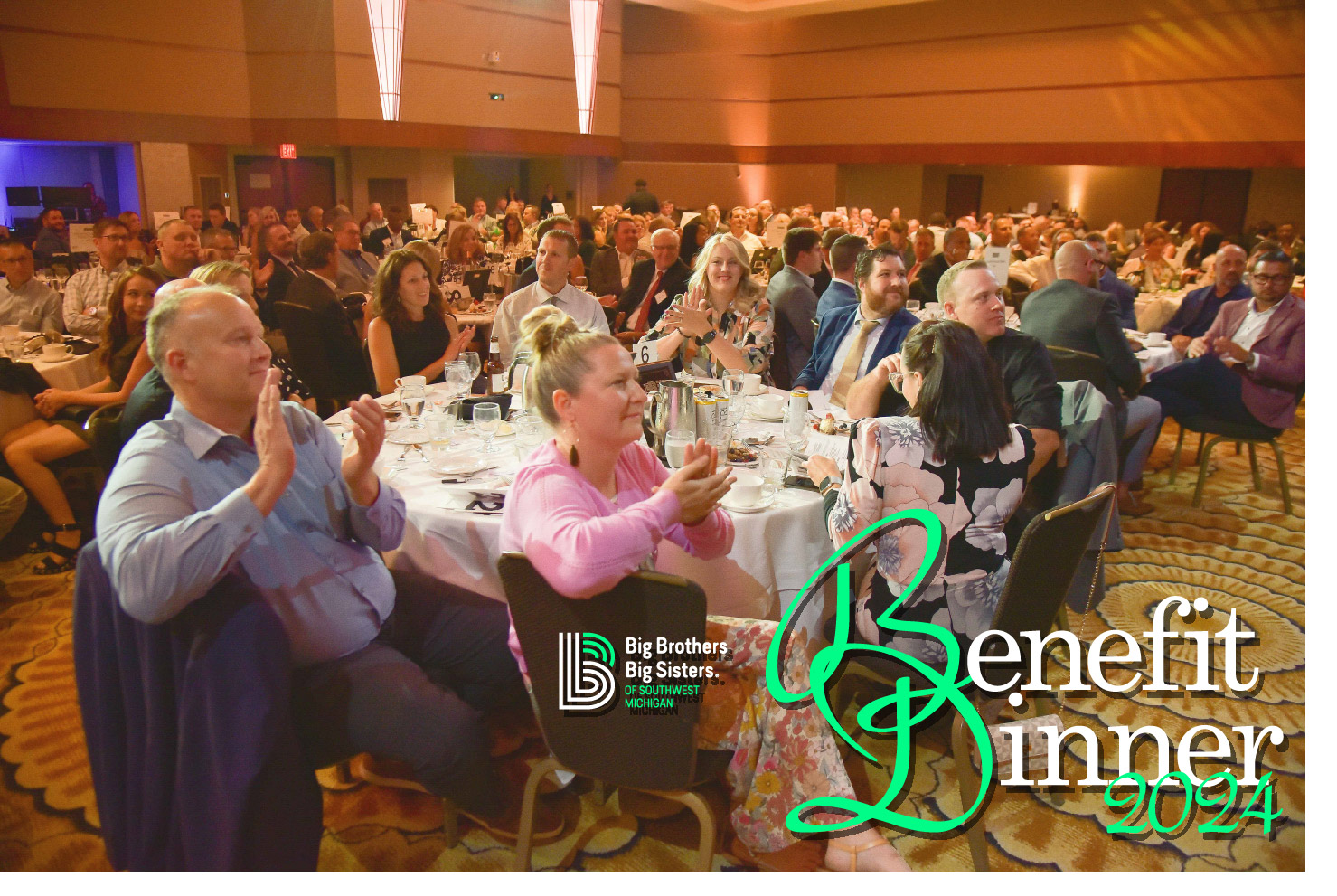 A crowd of people smiling and clapping inside of the Radisson's ballroom. In the lower right hand corner is the 2024 Benefit Dinner logo.