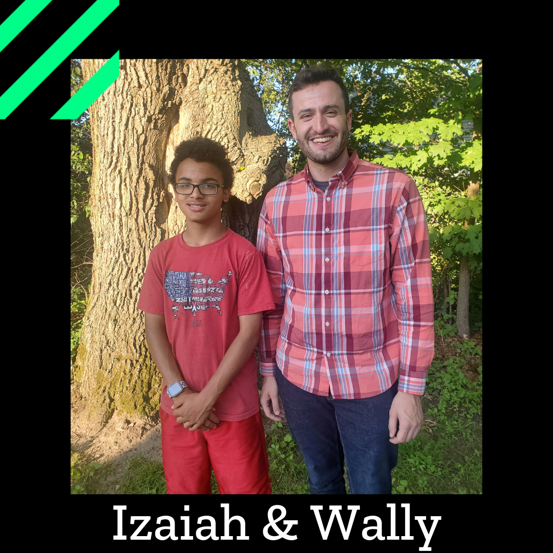 Izaiah and Wally stand outside near a tree, smiling at a camera.