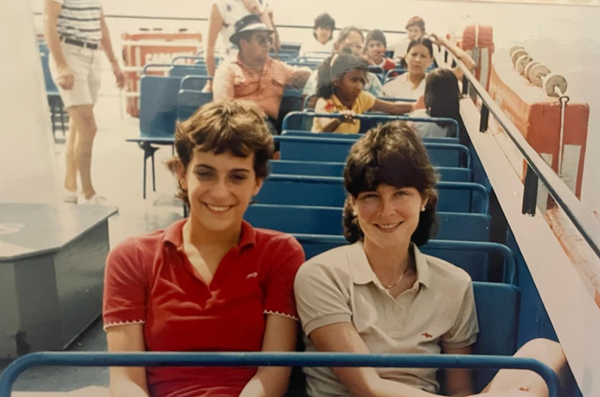 Maureen and Melissa sitting on a boat with blue seats, smiling at the camera.