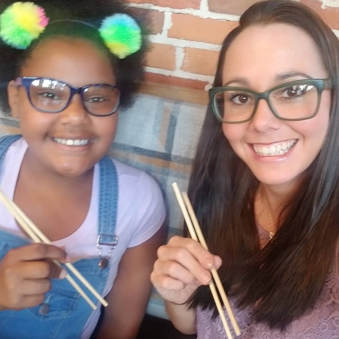 Codie and Aniyah, holding chopsticks and smiling at the camera.