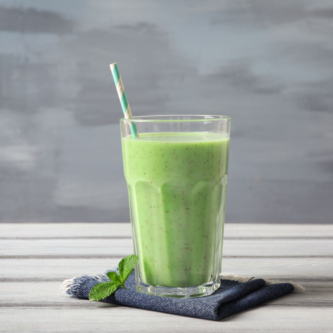 A green smoothie sitting on a wooden table with a gray background