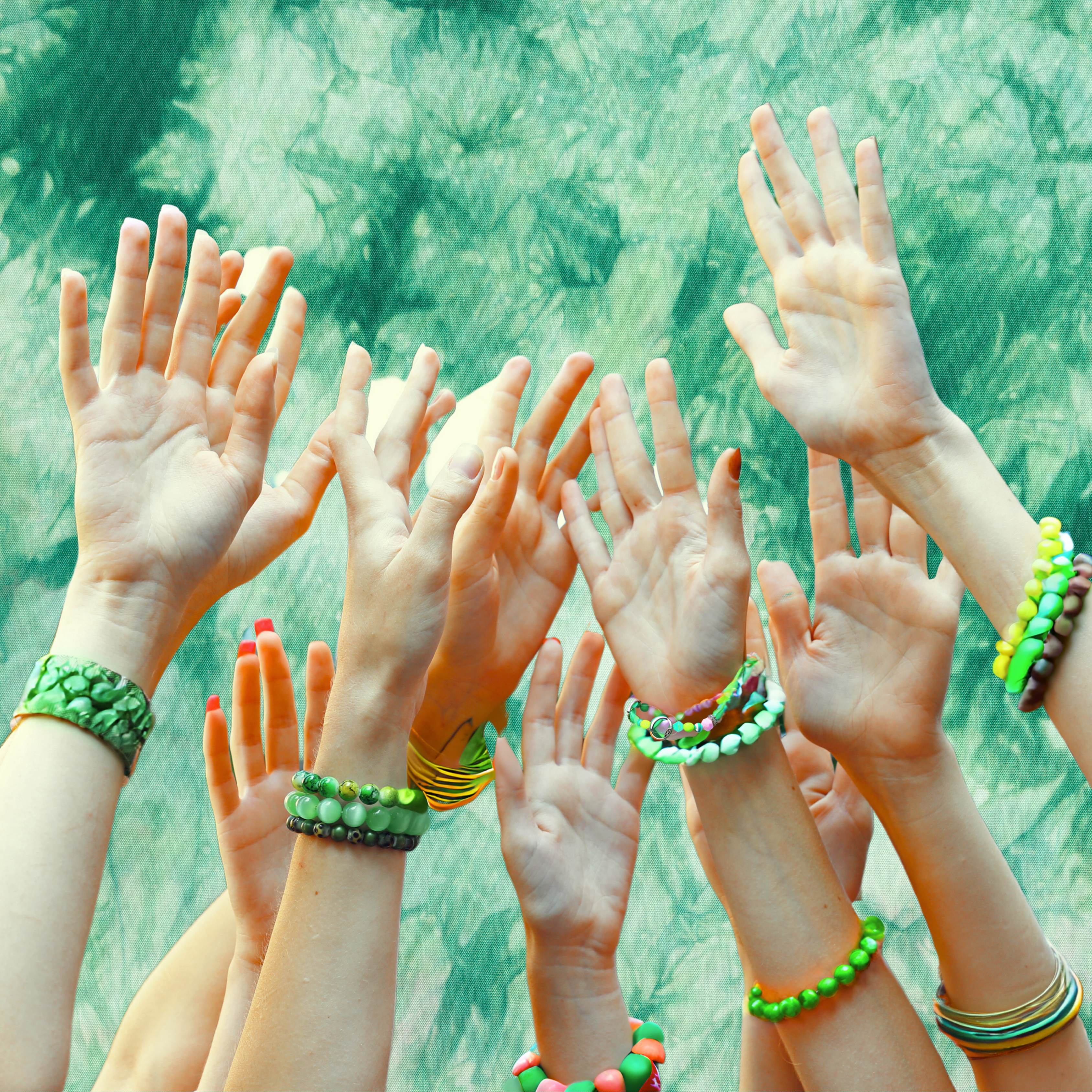 A group of hands reaching up to the sky with a green tye dye background and lots of green bracelets on the wrists