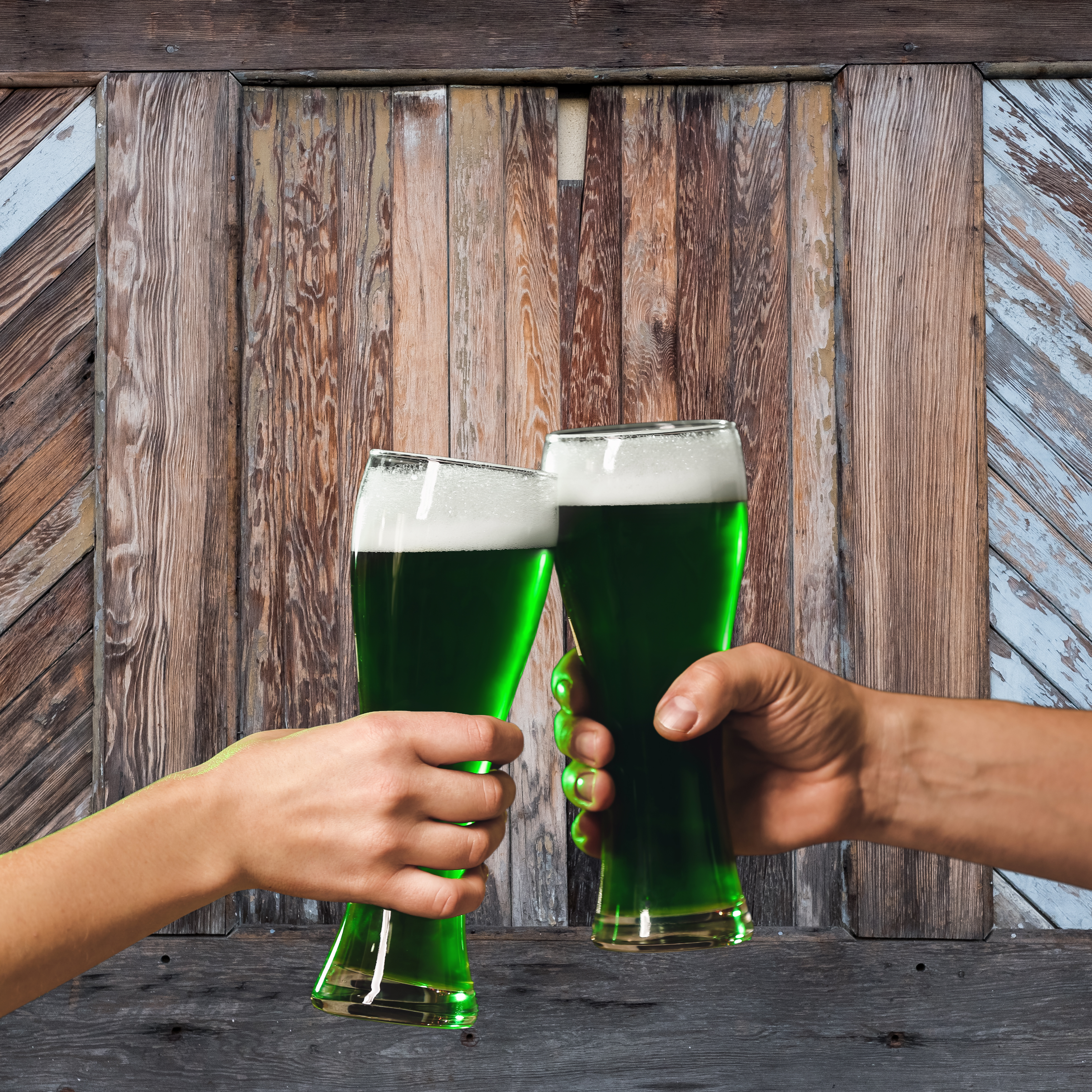 Two people cheering with green beer in their hands near a reclaimed wood wall or barn door