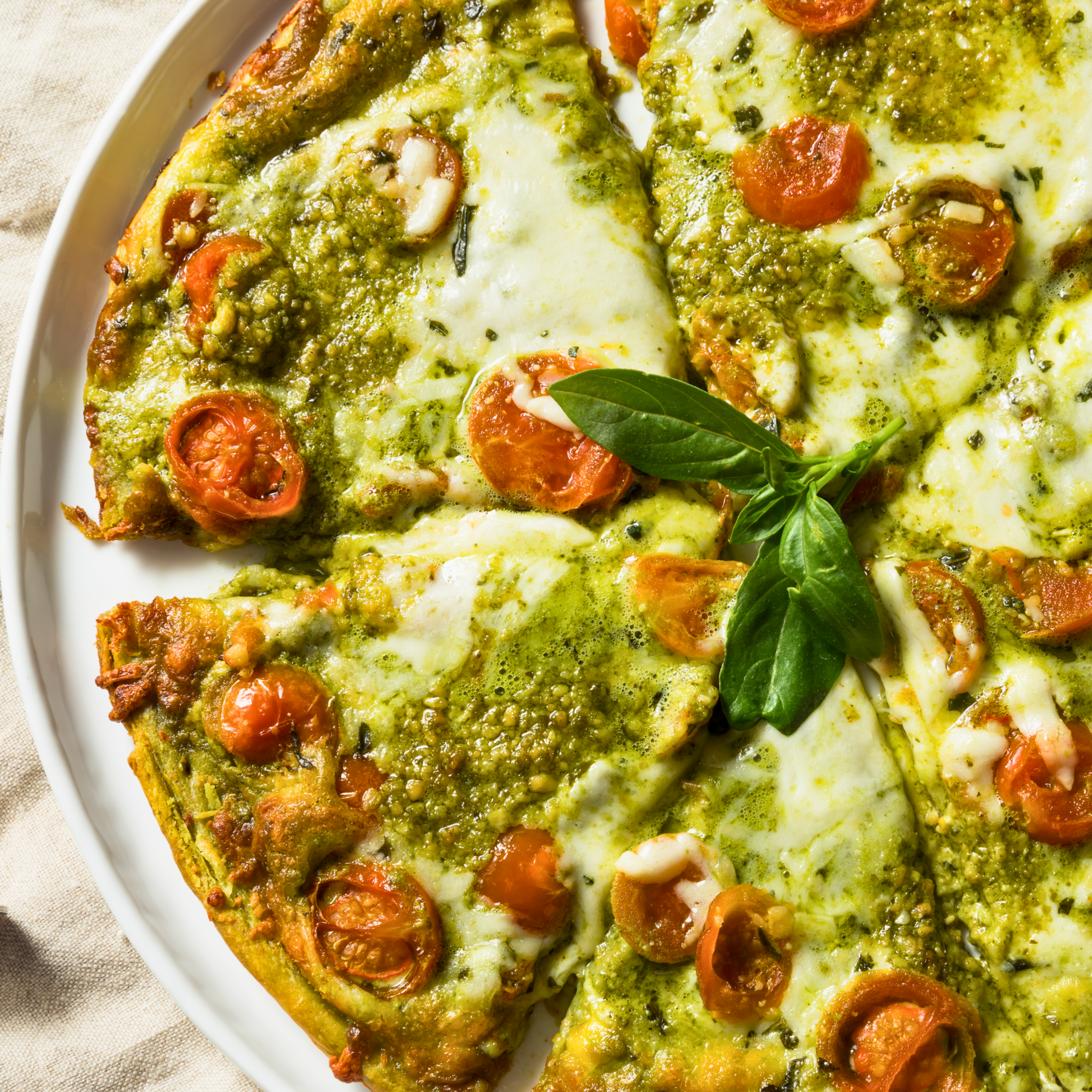 A photo of pesto pizza with basil in the middle