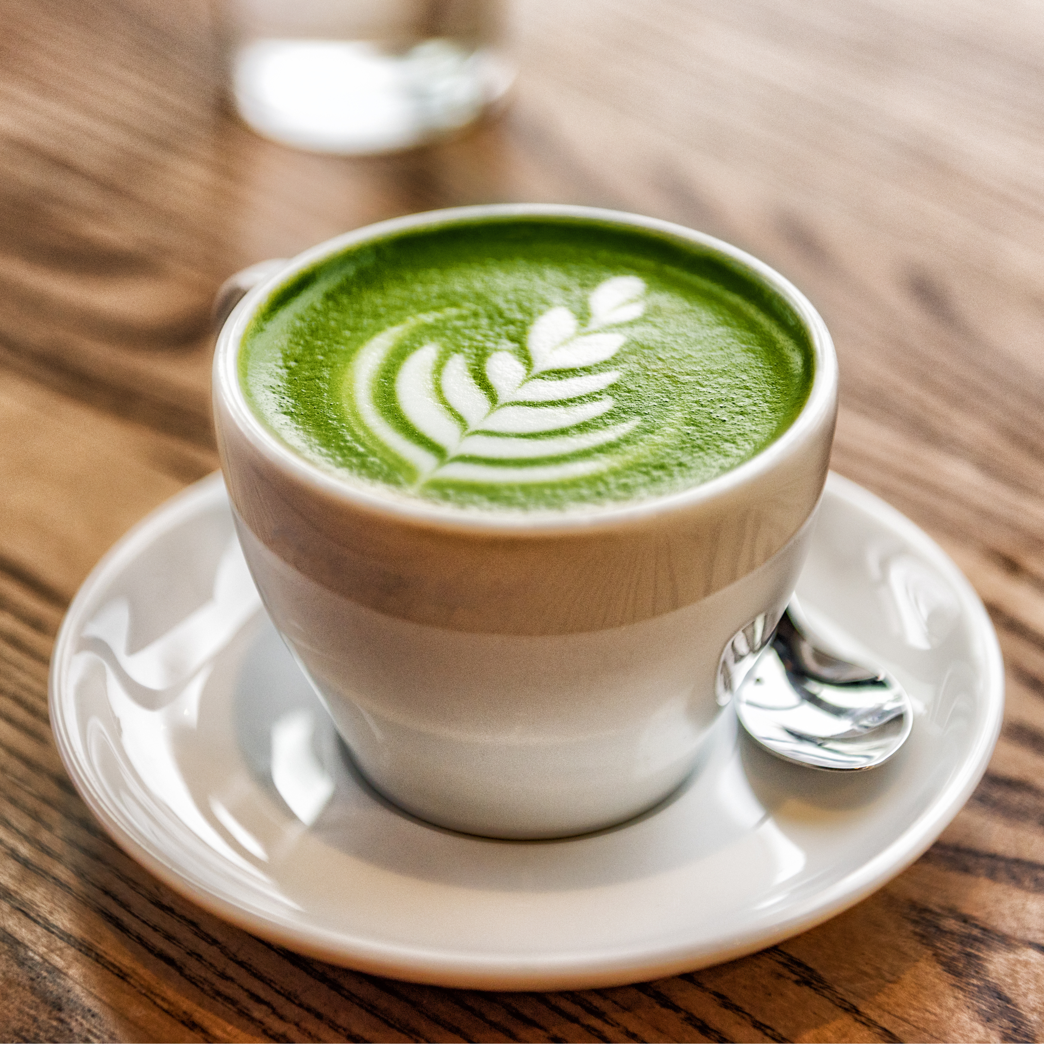 A green tea or coffee latte in a white ceramic mug on a wood table
